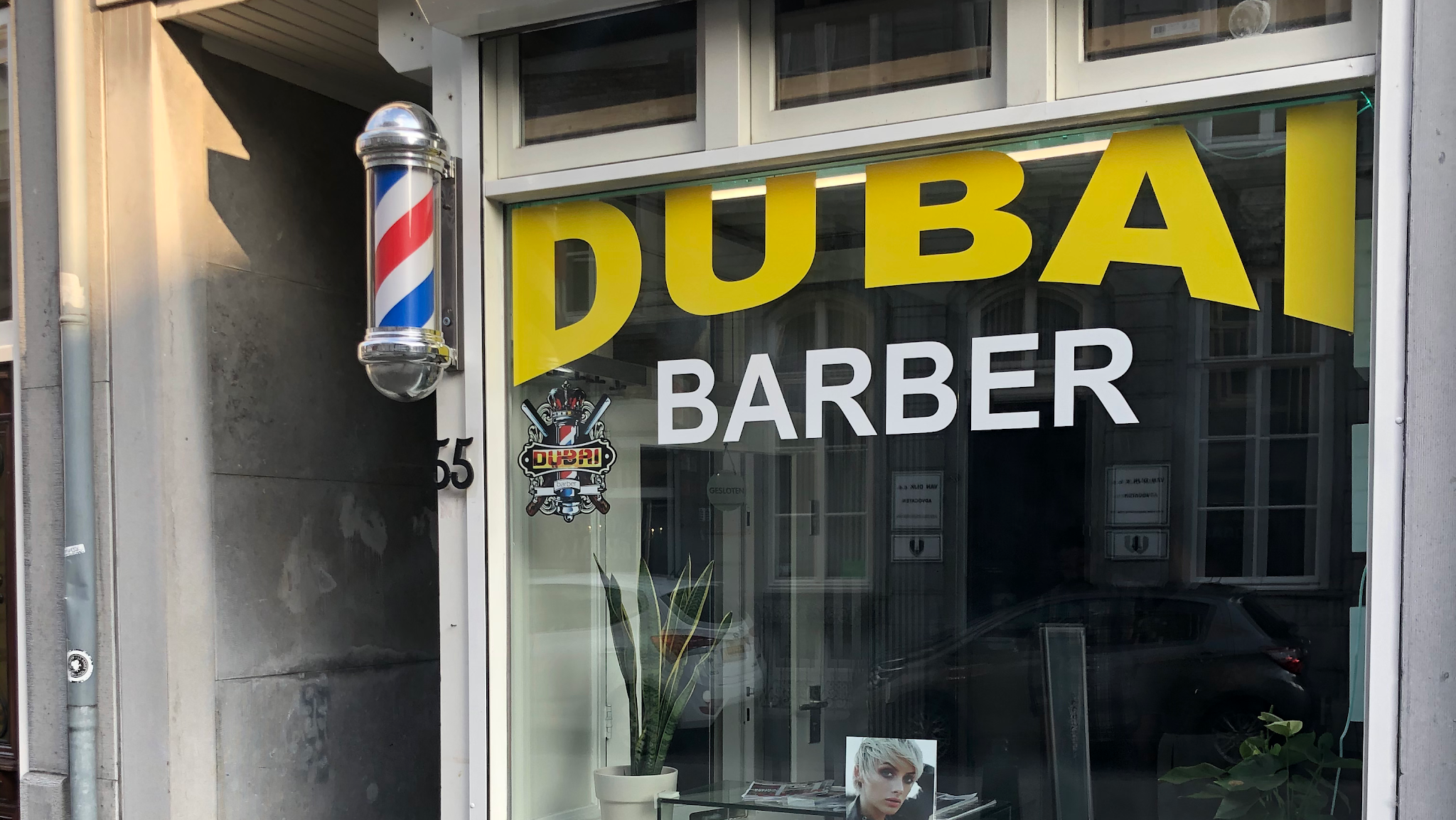 De etalage van Dubai Barber met gele letters en een kapperspaal aan de Hoogbrugstraat